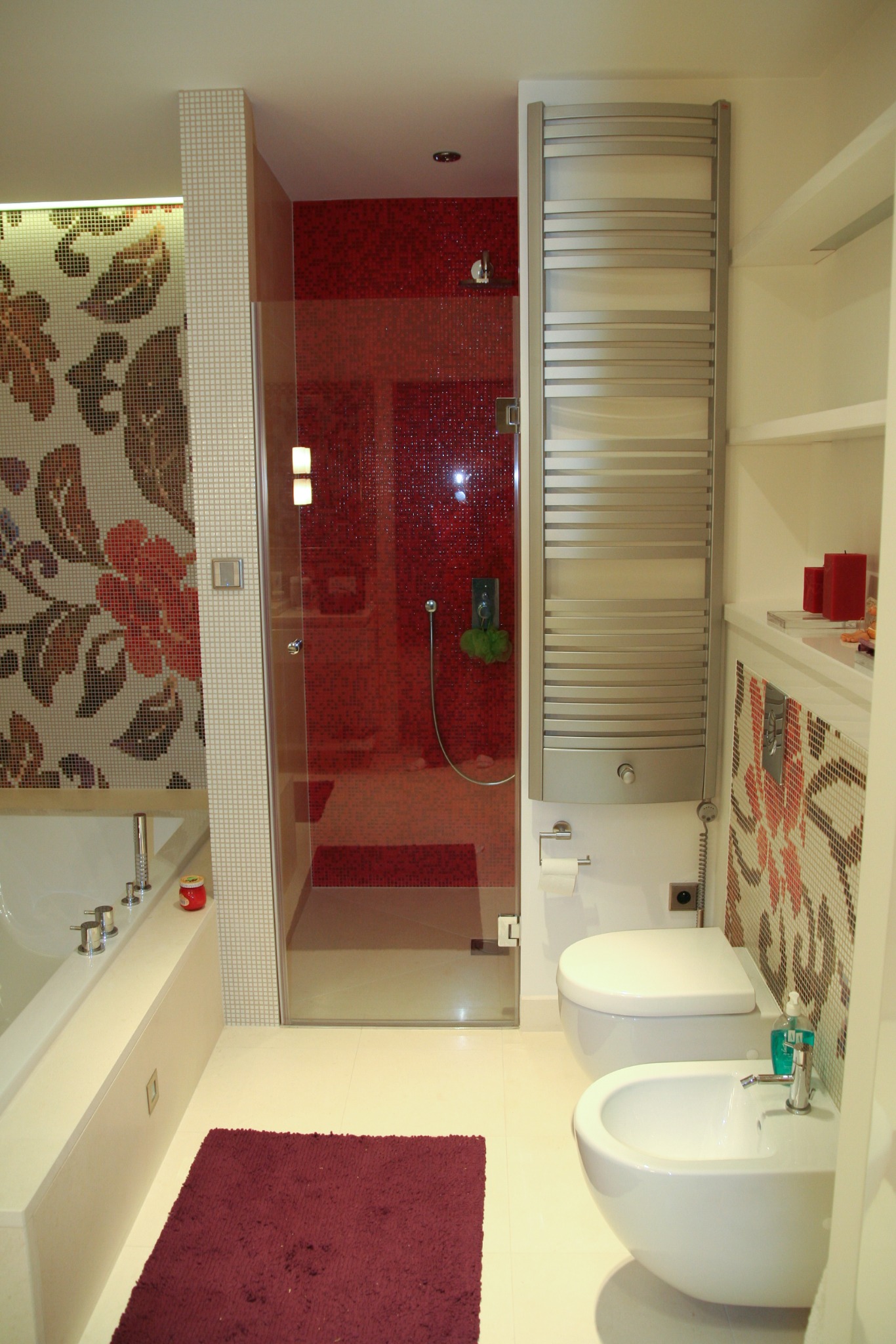 Nowoczesna łazienka z mozaiką kwiatową, kabiną prysznicową z czerwonymi płytkami i grzejnikiem drabinkowym, uzupełniona fioletowym dywanikiem.