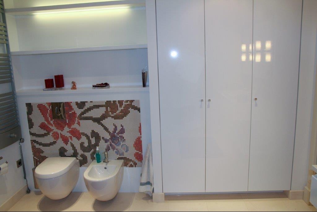 Nowoczesna łazienka w Warszawie z białą armaturą, mozaiką kwiatową nad toaletą i bidetem oraz szafkami w zabudowie.