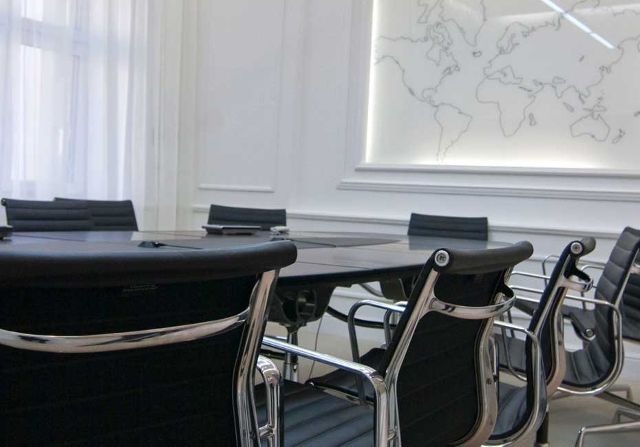 Elegancka sala konferencyjna z czarnym stołem i krzesłami na chromowanych nogach, tło stanowi biała ściana z konturową mapą świata.