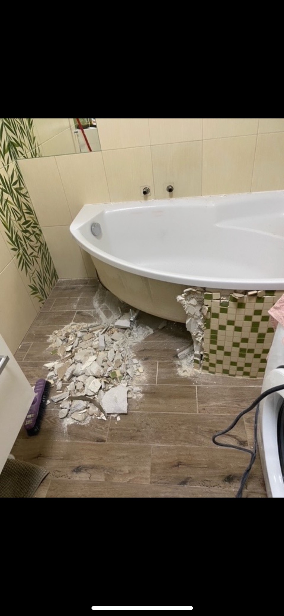 Demontaż obudowy wanny z mozaiki, widoczne gruz i narzędzia na podłodze wyłożonej panelami imitującymi drewno.