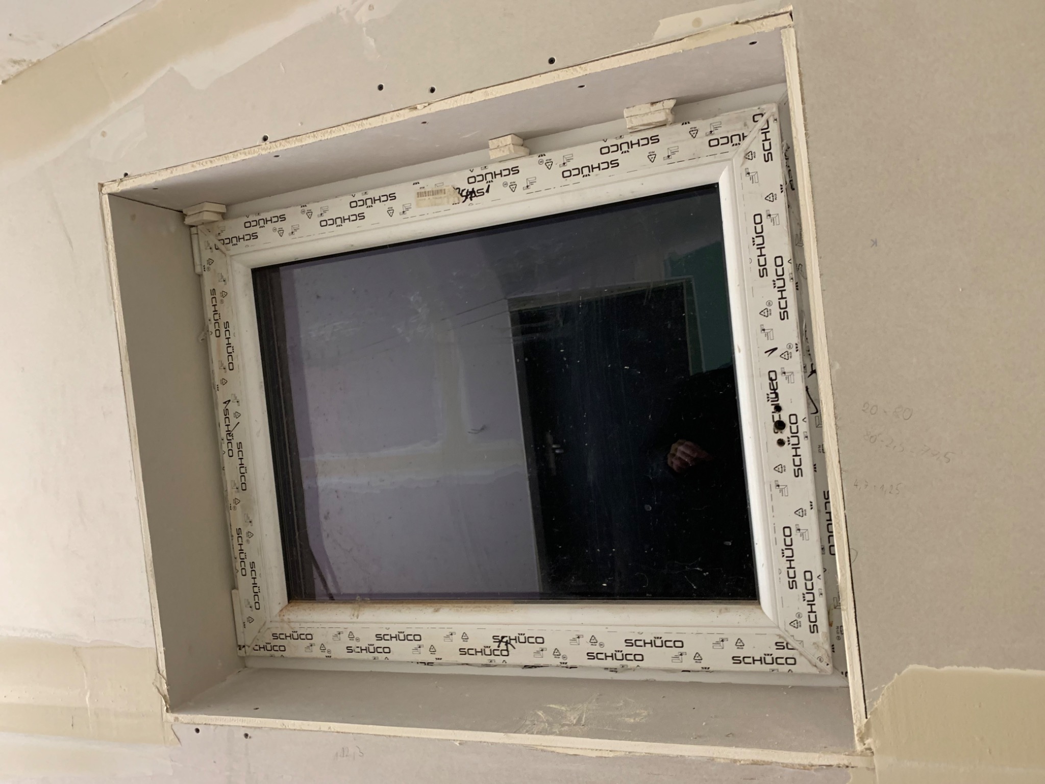 Okno PCV marki Schuco zamontowane w surowym otworze, ściany w trakcie szpachlowania i przygotowania do malowania.