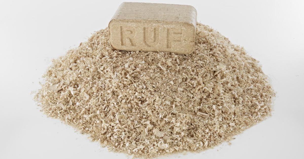 Brykiet drzewny RUF leżący na kupce wiórów drzewnych na białym tle.