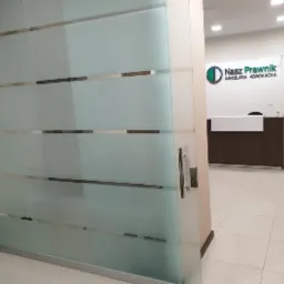 Szklane drzwi wejściowe do kancelarii prawnej z widocznym logo firmy 'Nasz Prawnik' i recepcją w tle.