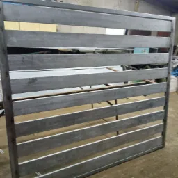 Surowa, spawana konstrukcja metalowa ogrodzenia panelowego z poziomymi szczeblami, widoczna w warsztacie, przed malowaniem.