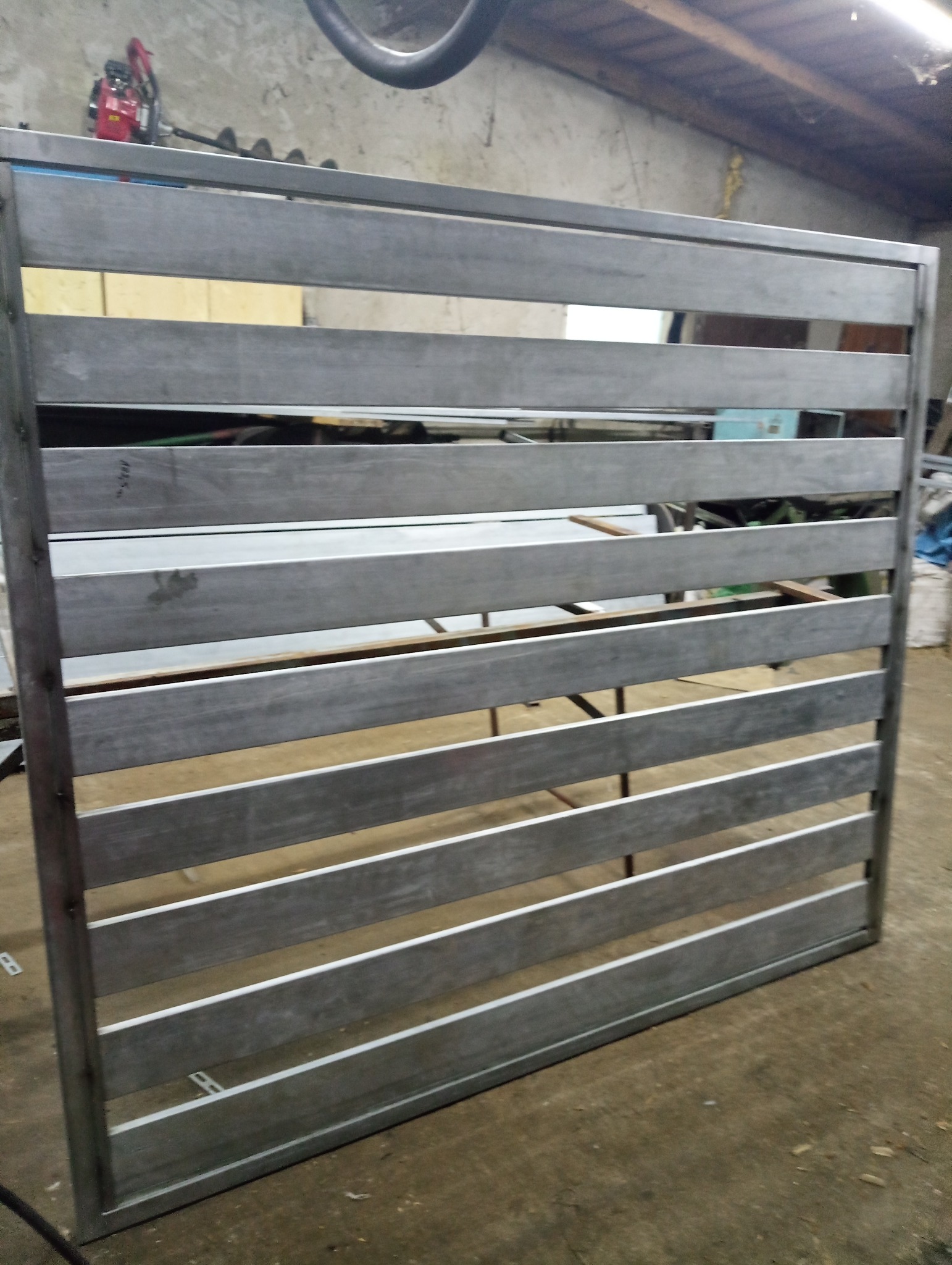 Surowa, spawana konstrukcja metalowa ogrodzenia panelowego z poziomymi szczeblami, widoczna w warsztacie, przed malowaniem.