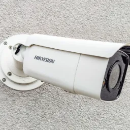 Kamera monitoringu marki Hikvision zamontowana na szarej, teksturowanej ścianie zewnętrznej budynku.