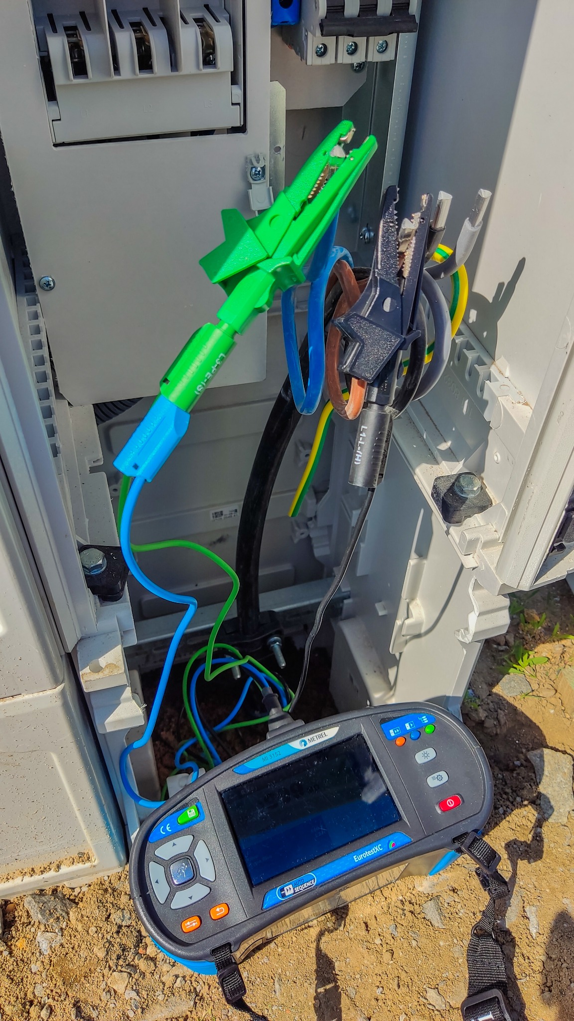 Miernik elektryczny EurotestXC firmy Metrel podłączony klemami krokodylkowymi do przewodów w skrzynce rozdzielczej podczas pomiarów.