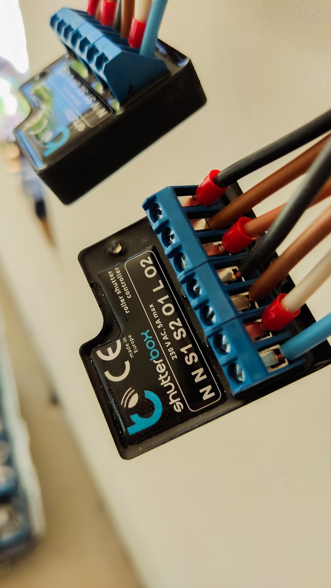 Zbliżenie na podłączone przewody do niebieskiej listwy zaciskowej regulatora rolet, widoczny napis 'shutterbox' i oznaczenia 230 V AC, 5A max.