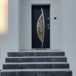 Nowoczesna elewacja domu z białym tynkiem, ciemnymi drzwiami wejściowymi z ozdobnym przeszkleniem i schodami z szarej kostki brukowej prowadzącymi do wejścia.