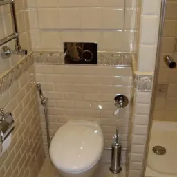 Wykończona łazienka w beżowych płytkach metra z chromowanymi akcentami, widoczny sedes, bidetka i grzejnik drabinkowy.