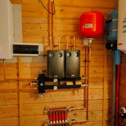 Sergii Cholavyn - Kompleksowa instalacja grzewcza z kotłem, zbiornikami i rozdzielaczem, zamontowana na drewnianej ścianie z boazerii.