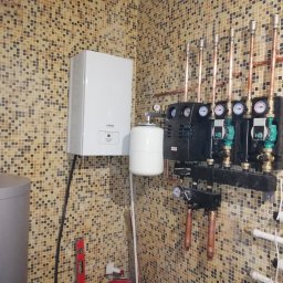 Sergii Cholavyn - Kotłownia z piecem gazowym Viessmann Vitocell 100 i rozbudowaną instalacją hydrauliczną z miedzianymi rurami na ścianie wyłożonej mozaiką.