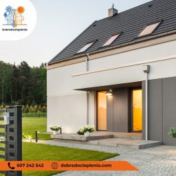 Dobredocieplenia - Nowoczesny dom jednorodzinny z szarą elewacją, oświetlonym wejściem i zadbanym trawnikiem, widok z niskiej perspektywy.