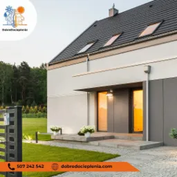 Nowoczesny dom jednorodzinny z szarą elewacją, oświetlonym wejściem i zadbanym trawnikiem, widok z niskiej perspektywy.