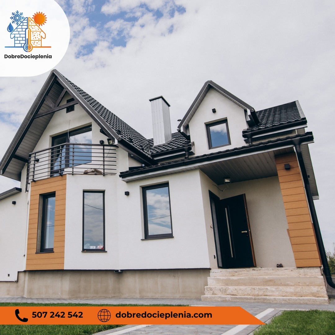 Dwukondygnacyjny dom jednorodzinny z białą elewacją, ciemną stolarką okienną i drewnopodobnymi panelami, widoczny z dołu pod kątem na tle błękitnego nieba z chmurami.