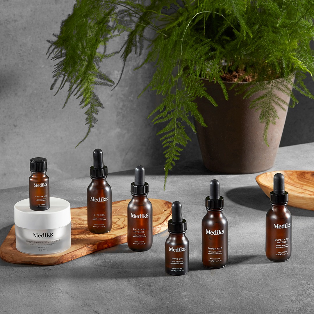Zestaw kosmetyków marki Medik8 z witaminą C, w tym serum i krem, zaprezentowany na drewnianej desce na tle szarej powierzchni i zielonej rośliny doniczkowej, Bielsko-Biała.