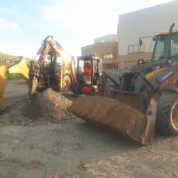 Praca koparek i ładowarki Volvo BL71B na placu budowy podczas wykopu ziemi, widoczny operator w pomarańczowej kamizelce odblaskowej.