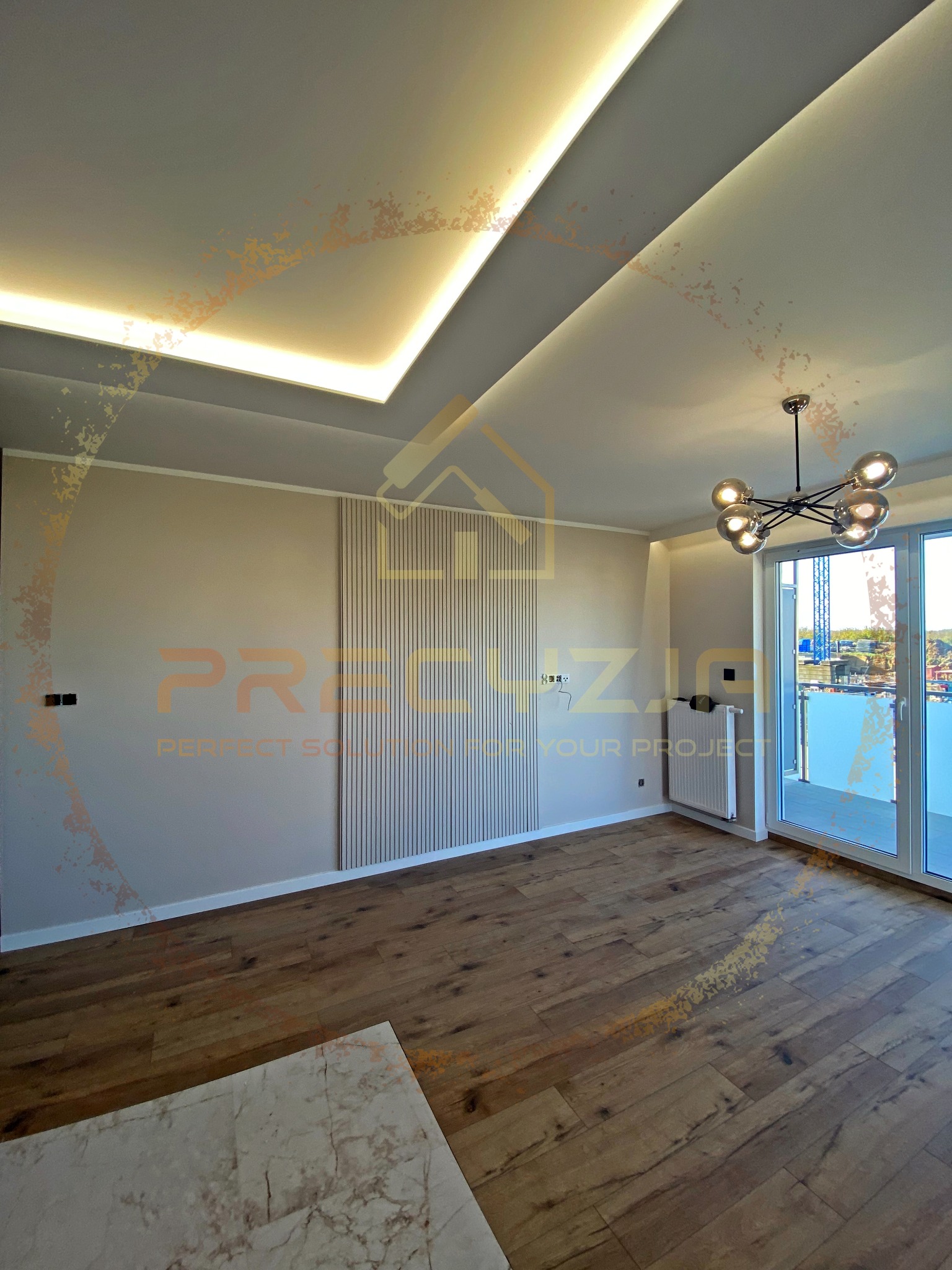 Jasne, przestronne wnętrze z drewnianą podłogą, panelami ściennymi z pionowymi listwami, nowoczesną lampą sufitową i oknami balkonowymi z widokiem na zewnątrz. Sufit podwieszany z oświetleniem LED.