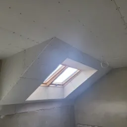 Montaż płyt na skośnym poddaszu z oknem dachowym, widoczne ślady po wkrętach, ściany przygotowane pod wykończenie.