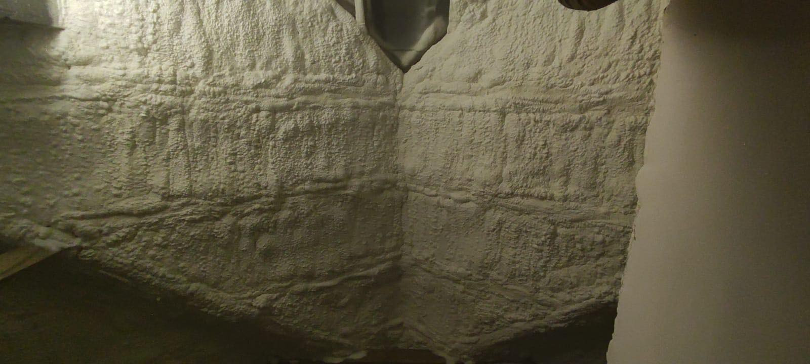 Poddasze ocieplone pianką PUR, widoczne nierównomierne pokrycie i szczeliny w narożnikach, oświetlenie halogenowe.