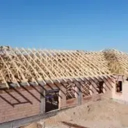 Budowa domu w stanie surowym otwartym: konstrukcja więźby dachowej na murach z czerwonej cegły, widok z góry w słoneczny dzień.