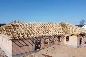 Budowa domu w stanie surowym otwartym: konstrukcja więźby dachowej na murach z czerwonej cegły, widok z góry w słoneczny dzień.