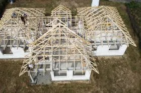 Wznoszenie konstrukcji drewnianej dachu na budynku w stanie surowym otwartym. Widoczne krokwie, murłaty i ekipa budowlana pracująca na wysokości.