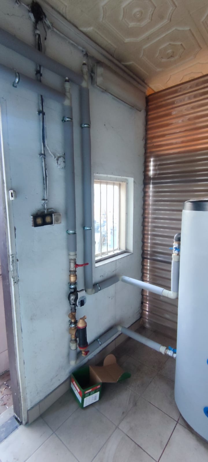 Instalacja rur grzewczych z zaworami i pompą obiegową w pomieszczeniu z oknem, widoczna skrzynka po filtrze.