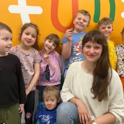 Uśmiechnięta nauczycielka z grupą dzieci na tle kolorowej ściany z motywami edukacyjnymi, tworząca przyjazną atmosferę w klasie językowej.