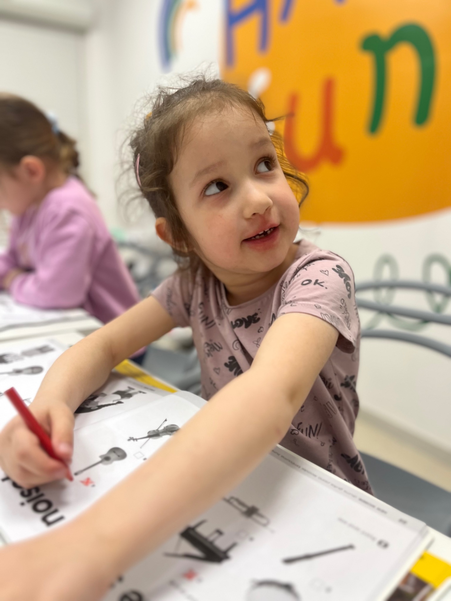 Dziewczynka z czerwoną kredką rozwiązuje zadanie z instrumentami muzycznymi na lekcji w jasnym, kolorowym pomieszczeniu.