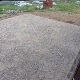 Nowo ułożona kostka granitowa zasypana piaskiem, widoczne przygotowane zapasy kostki i cegieł w tle, obrzeże wzdłuż budynku.