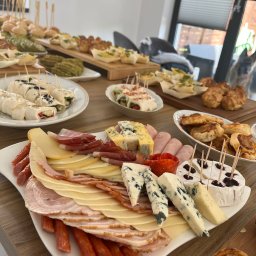 Ewelina Orłowska evela_cake - Bogato zastawiony stół z przekąskami w Chruszczobrodzie, prezentujący różnorodne sery, wędliny, roladki i mini-kanapeczki, gotowe do podania podczas imprezy.