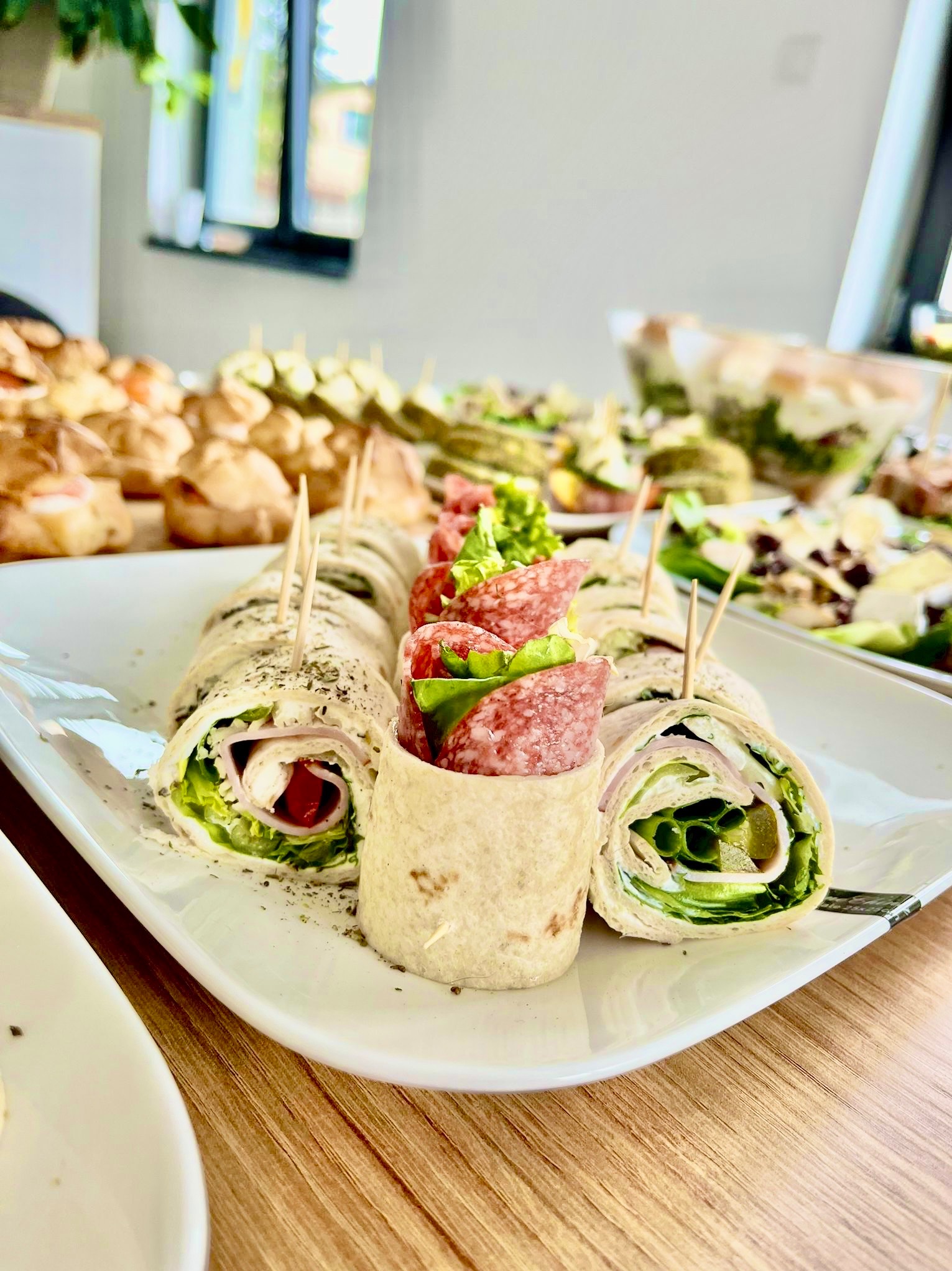 Tortilla wraps z szynką, serem, warzywami i salami na białym talerzu, zabezpieczone wykałaczkami, część zastawy cateringowej na stole.