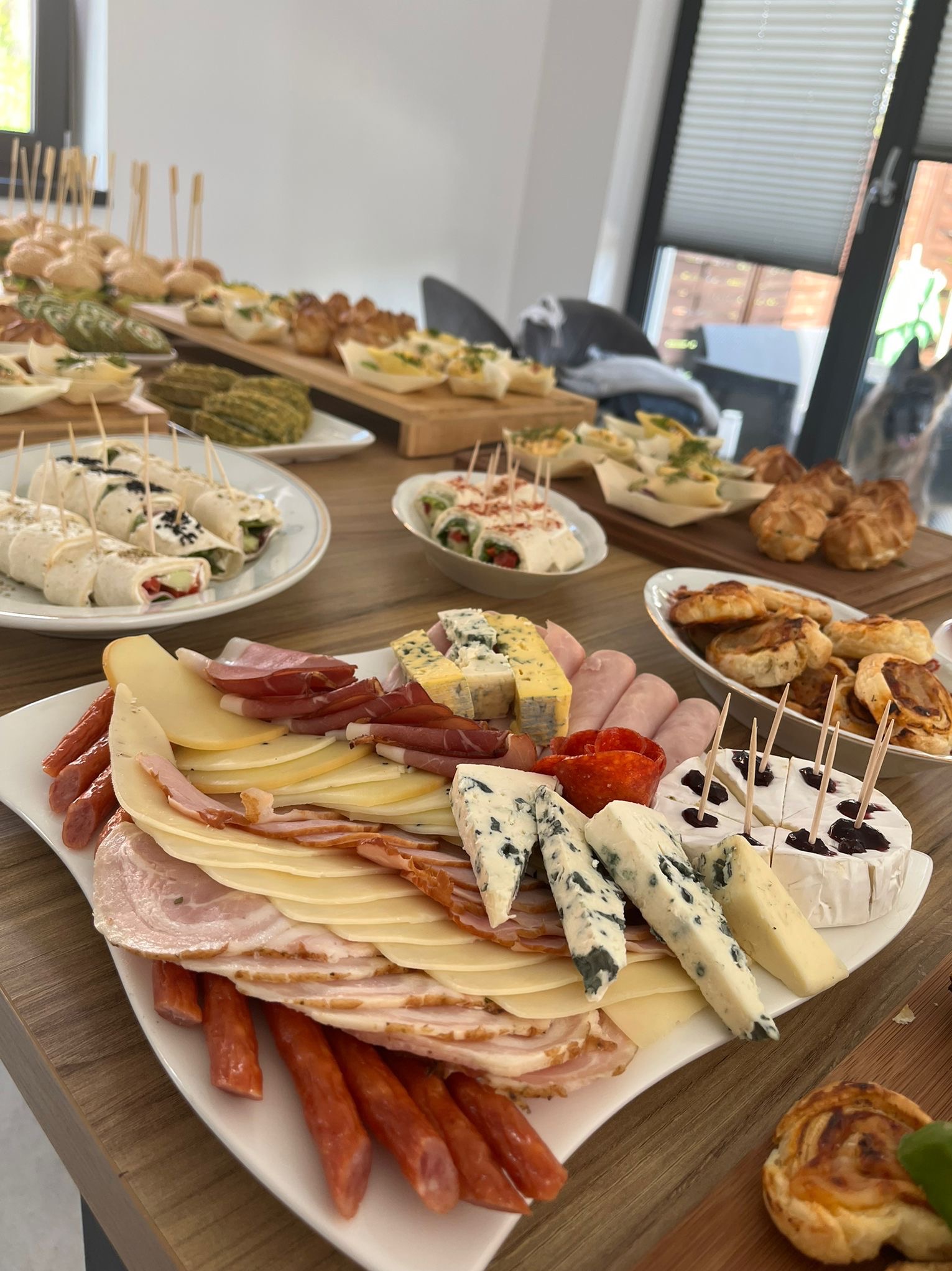 Bogato zastawiony stół z przekąskami w Chruszczobrodzie, prezentujący różnorodne sery, wędliny, roladki i mini-kanapeczki, gotowe do podania podczas imprezy.