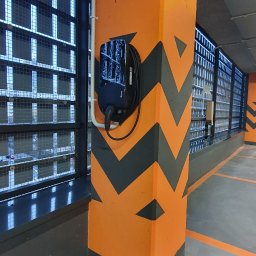 PC INSTAL - Stacja ładowania pojazdów elektrycznych marki Pure zamontowana na pomarańczowym filarze z szarymi chevronami w garażu podziemnym.