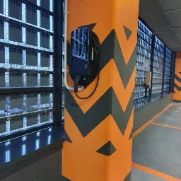 Stacja ładowania pojazdów elektrycznych marki Pure zamontowana na pomarańczowym filarze z szarymi chevronami w garażu podziemnym.