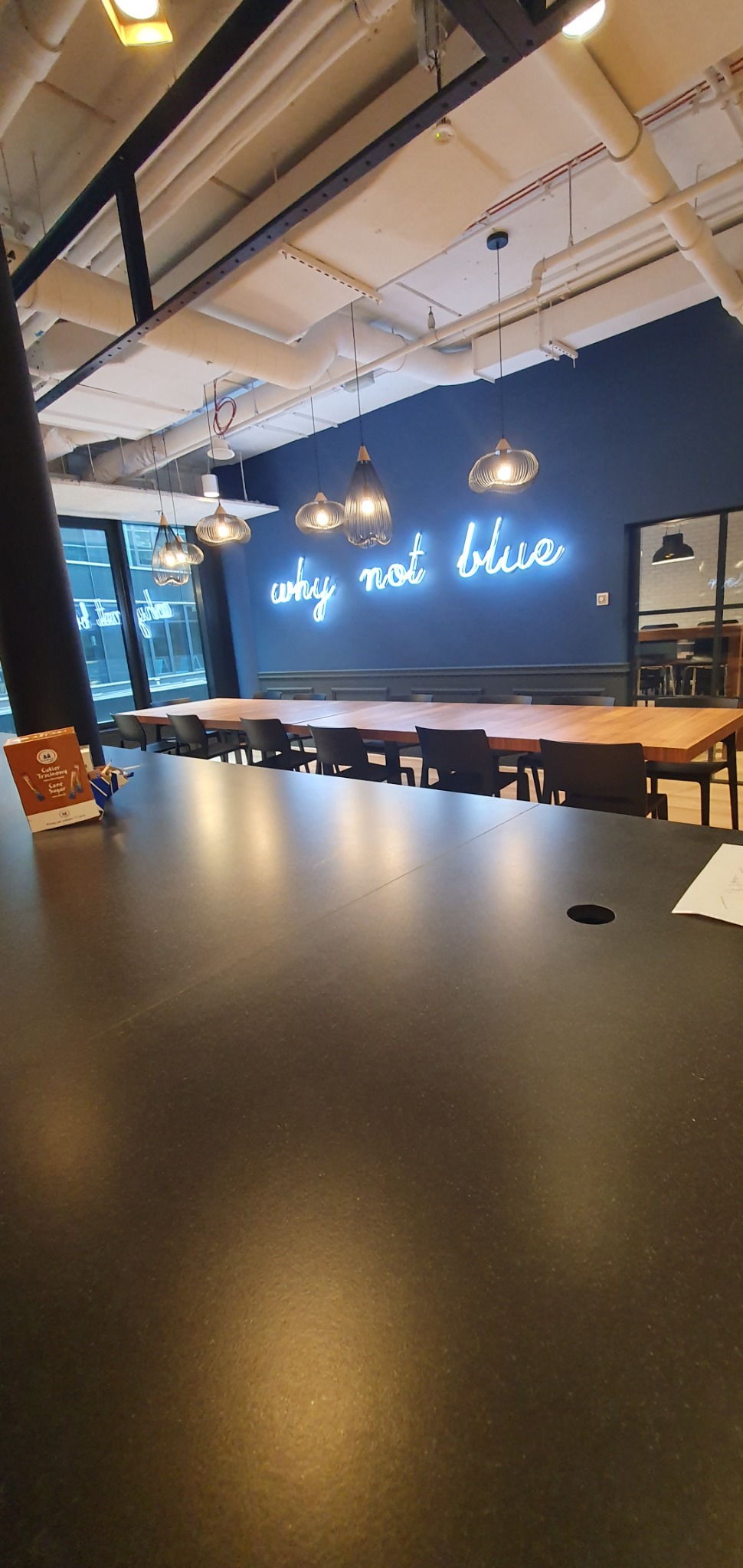 Wnętrze biura z długim stołem konferencyjnym, wiszącymi lampami i neonem 'why not blue' na niebieskiej ścianie.
