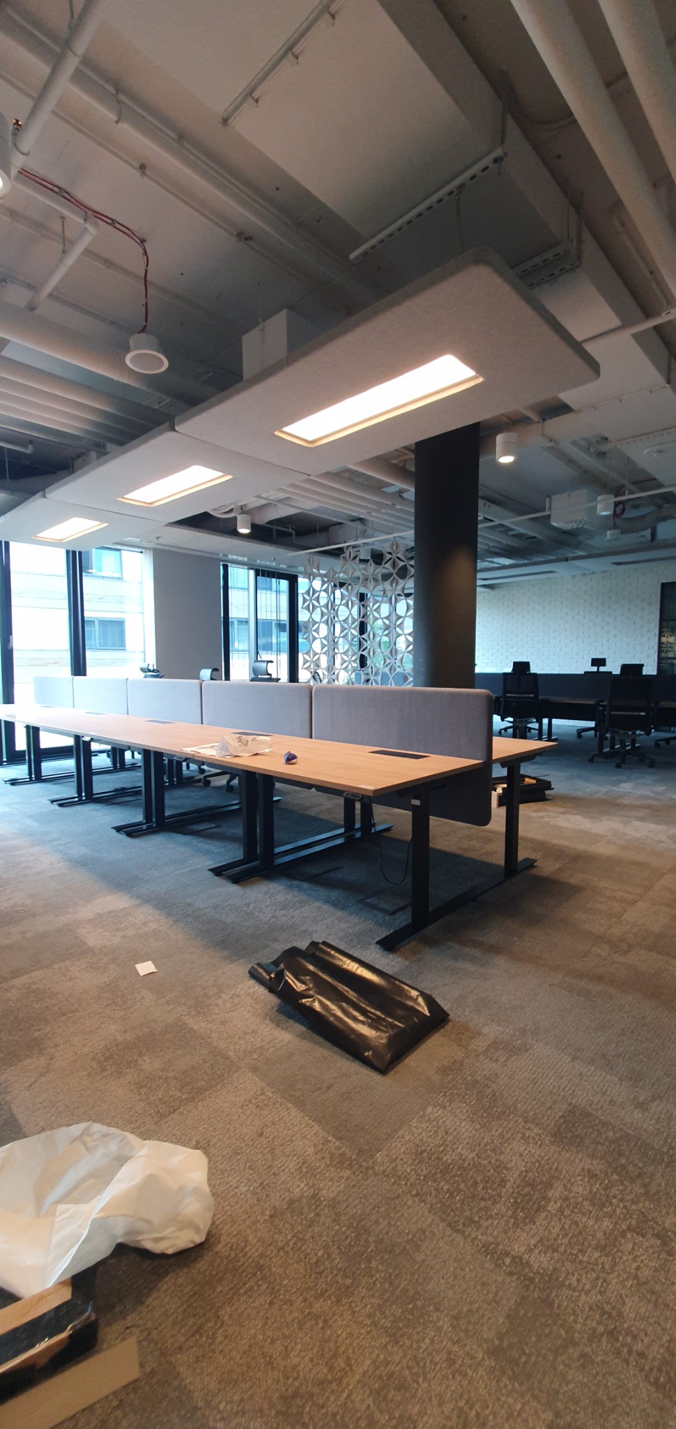 Biuro w trakcie przygotowań z zainstalowanym oświetleniem sufitowym LED, widoczne rozłożone kable i elementy montażowe na podłodze.