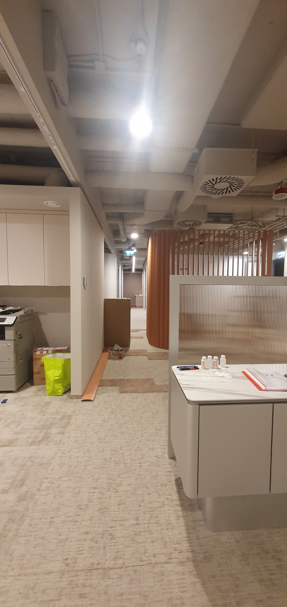 Wnętrze biurowe w trakcie prac instalacyjnych: widoczne kable pod sufitem, elementy oświetlenia i wentylacji, oraz materiały budowlane na podłodze.