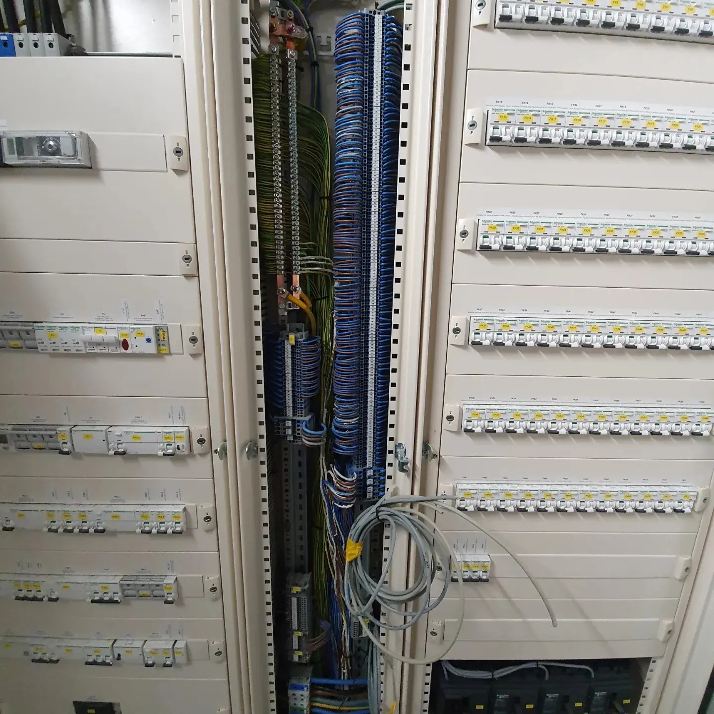 Otwarta szafa elektryczna z widocznymi zabezpieczeniami, przewodami i listwami zaciskowymi, kable ułożone w wiązki, widoczne elementy automatyki.