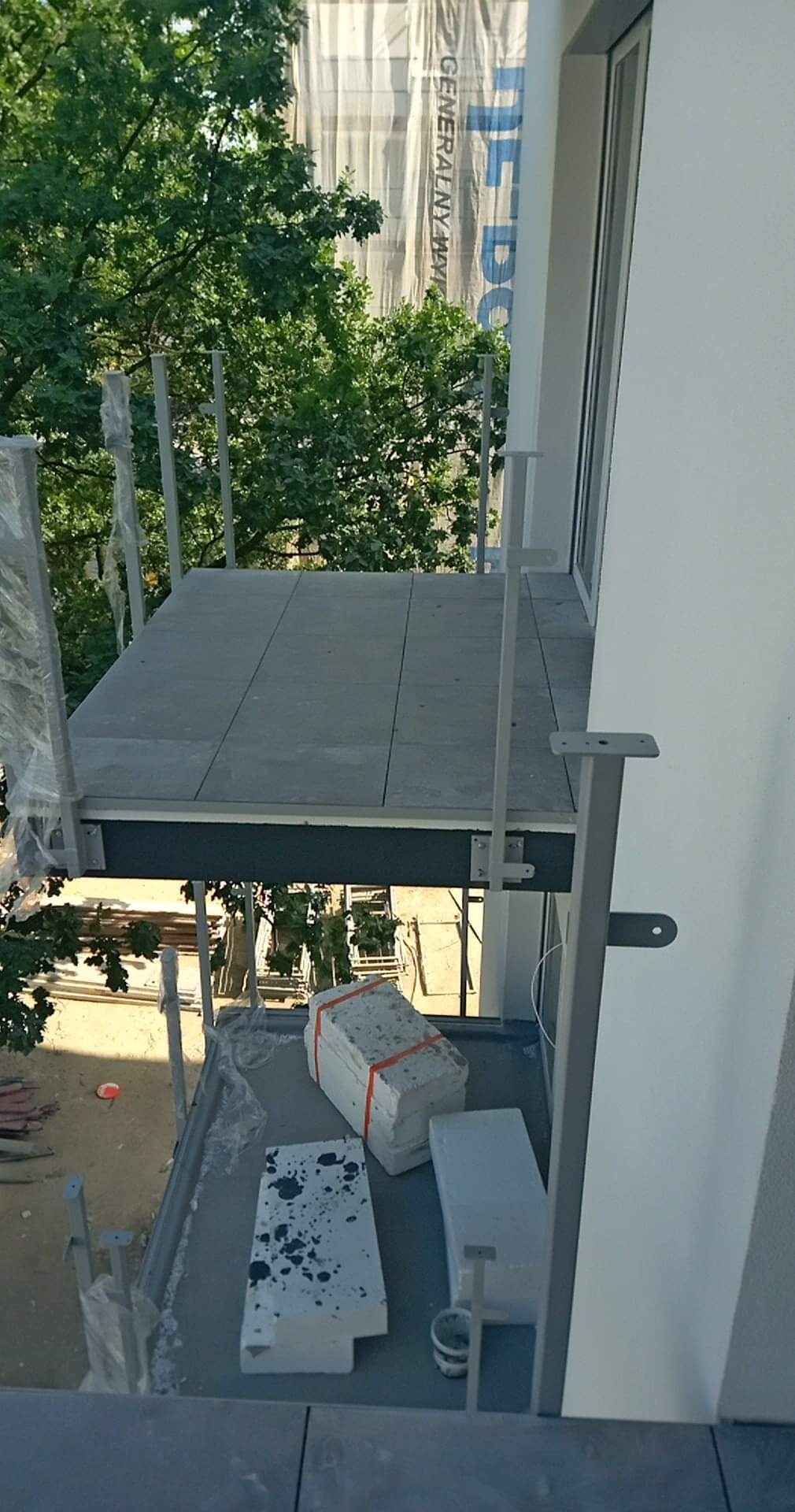 Montaż płytek na balkonie w trakcie realizacji, widoczne płyty ułożone na podłodze oraz materiały budowlane i elementy konstrukcyjne balkonu.