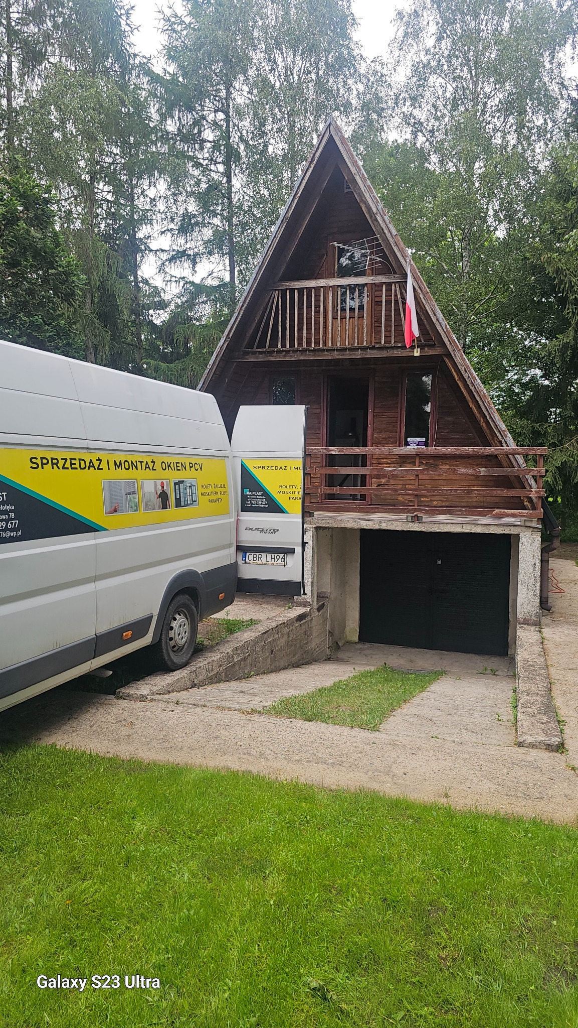 Montaż okien PCV w drewnianym domu typu A-frame, widoczny samochód dostawczy z reklamą firmy.