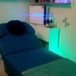 Niebieski stół do zabiegów z zielonym ręcznikiem w gabinecie z dekoracjami na ścianach i lampą emitującą niebieskie światło.