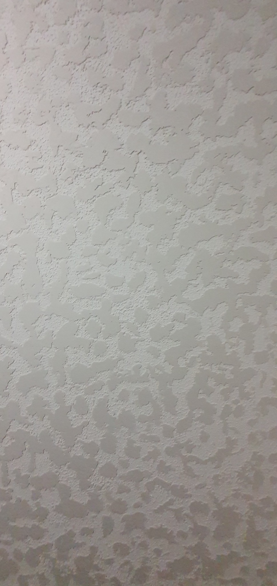 Szara, chropowata powierzchnia sufitu z wyraźną fakturą, przypominająca baranek, oświetlona z boku, ukazująca nierównomierne cieniowanie.