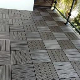 Modułowa podłoga tarasowa z desek kompozytowych ułożona w szachownicę, widok z góry na balkon z przeszkloną balustradą.