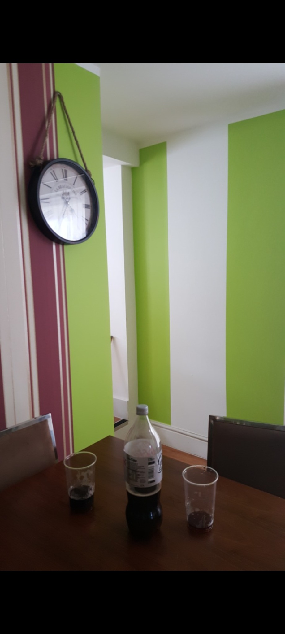 Wnętrze pokoju w Rastatt z pomalowanymi ścianami w pionowe pasy w kolorach zieleni, bieli i bordo, widoczny zegar na ścianie, stół z butelką i dwoma szklankami.