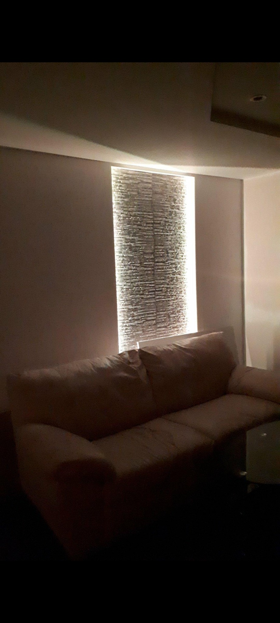 Salon z podświetloną ścianą dekoracyjną z kamienia, sofa w odcieniach beżu.