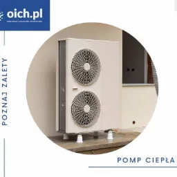 Zewnętrzna jednostka pompy ciepła zamontowana na betonowej podstawie z widocznymi białymi podkładkami antywibracyjnymi, na tle beżowej ściany budynku z oknem.