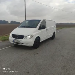 Biały Mercedes Vito z czarnymi felgami stoi na skrzyżowaniu polnych dróg pod pochmurnym niebem. Widoczne pole w tle.