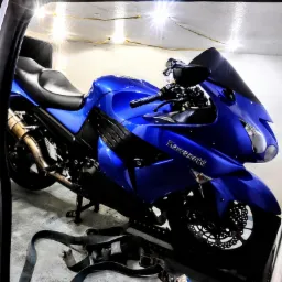 Błyszczący, niebieski motocykl Kawasaki zabezpieczony pasami transportowymi wewnątrz pojazdu, oświetlony dekoracyjnymi lampkami.